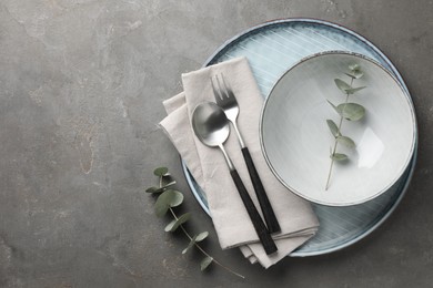 Stylish setting with cutlery, napkin, eucalyptus branches and plate on grey table, top view. Space for text