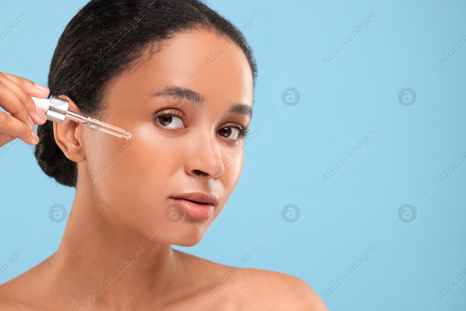 Photo of Beautiful woman applying serum onto her face on light blue background. Space for text