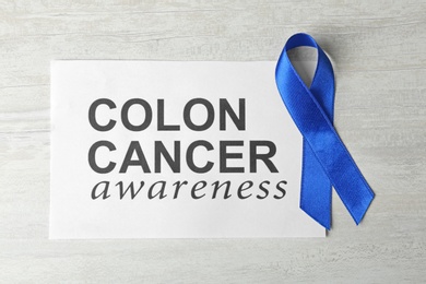 Photo of Paper with blue ribbon and text Colon cancer awareness on wooden background, top view