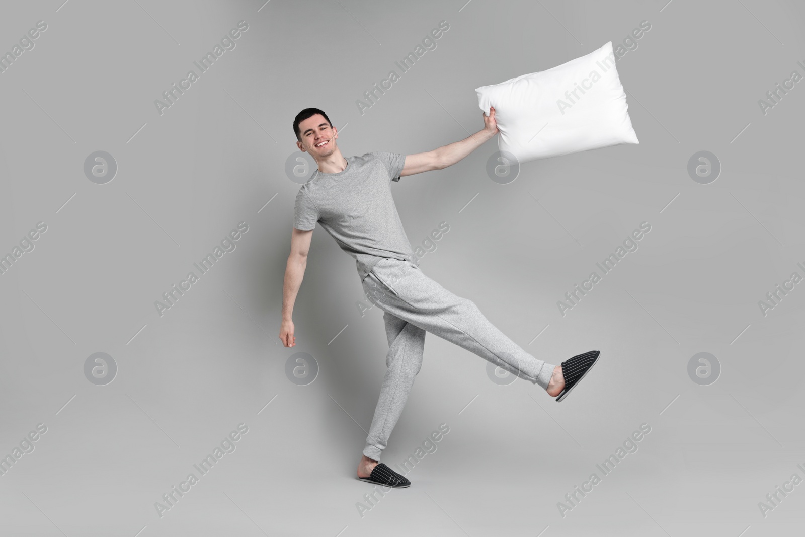 Photo of Happy man in pyjama holding pillow on grey background