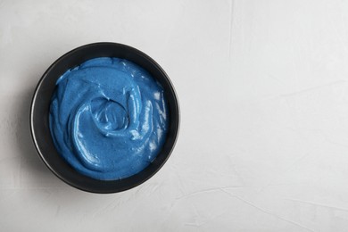 Photo of Bowl of cream with blue food coloring on light table, top view. Space for text