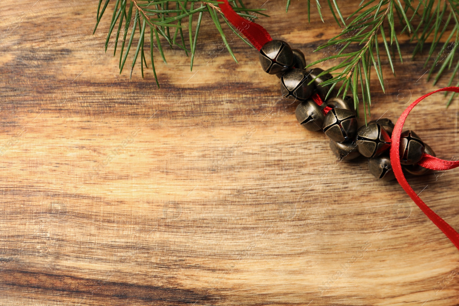 Photo of Metal sleigh bells on wooden table, flat lay. Space for text