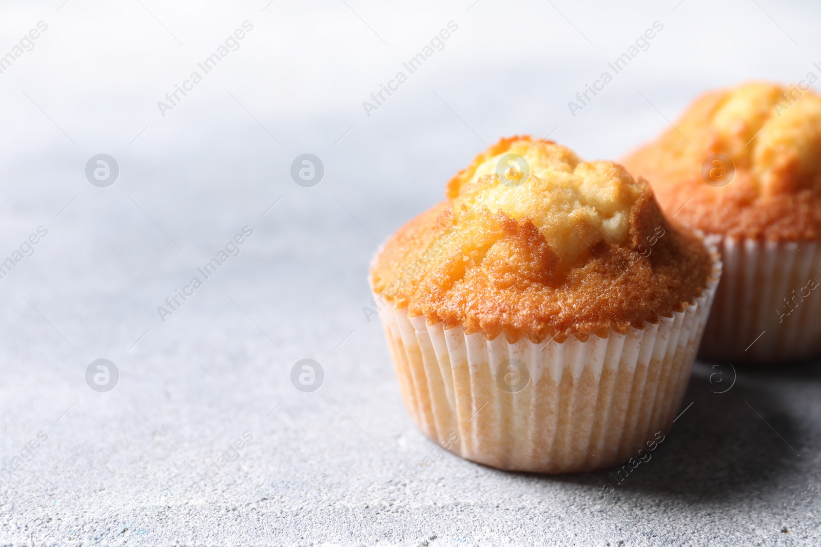 Photo of Delicious sweet muffins on light grey textured table, closeup. Space for text