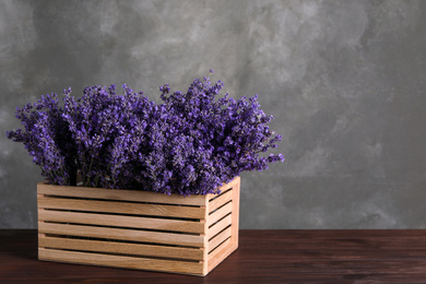 Photo of Beautiful lavender flowers in crate on wooden table against grey background. Space for text