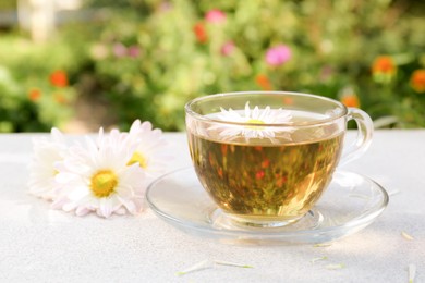 Glass cup of delicious chamomile tea on white table outdoors