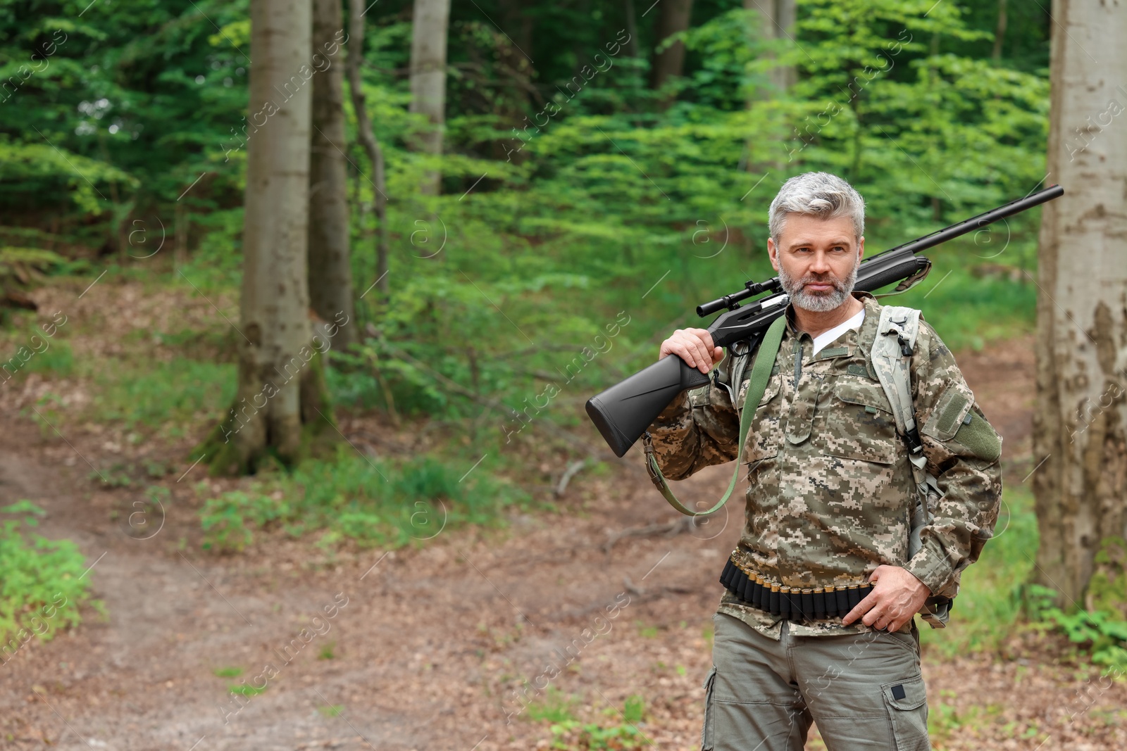 Photo of Man with hunting rifle wearing camouflage in forest. Space for text