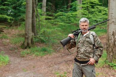 Man with hunting rifle wearing camouflage in forest. Space for text