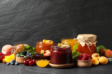 Photo of Jars with different jams and fresh fruits on black table