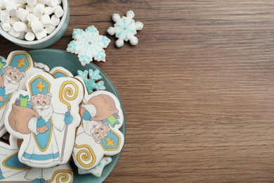 Tasty gingerbread cookies and cup of hot drink on wooden table, flat lay with space for text. St. Nicholas Day celebration