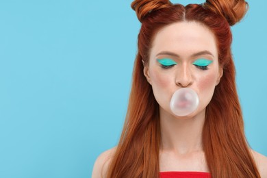 Beautiful woman with bright makeup and closed eyes blowing bubble gum on light blue background. Space for text