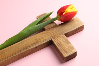 Easter - celebration of Jesus resurrection. Wooden cross and tulip on pink background, closeup
