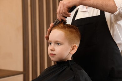 Professional hairdresser brushing boy's hair in beauty salon