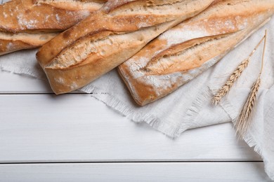 Photo of Tasty baguettes and spikelets on white wooden table, flat lay. Space for text