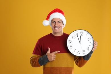 Photo of Man in Santa hat with clock on yellow background. New Year countdown