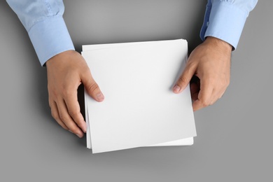 Photo of Man holding blank paper sheets for brochure at grey table, top view. Mock up