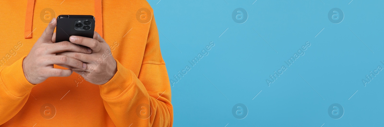 Image of Man typing message on mobile phone against light blue background, closeup. Banner design with space for text