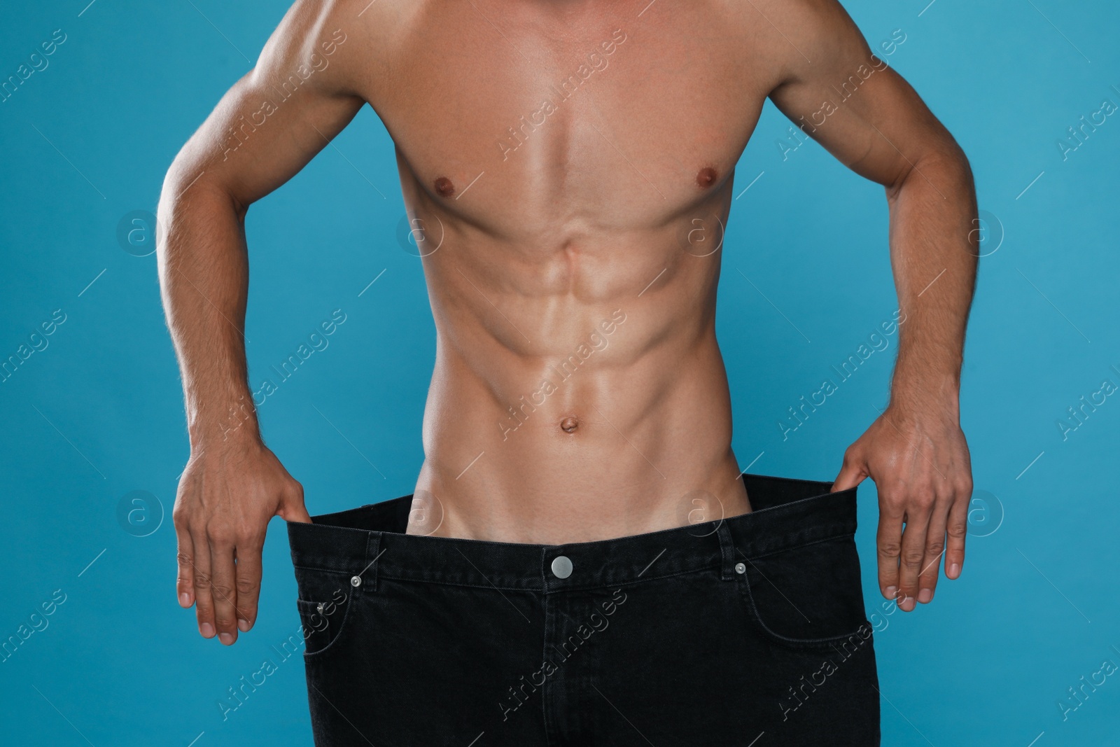 Photo of Shirtless man with slim body wearing big jeans on light blue background, closeup