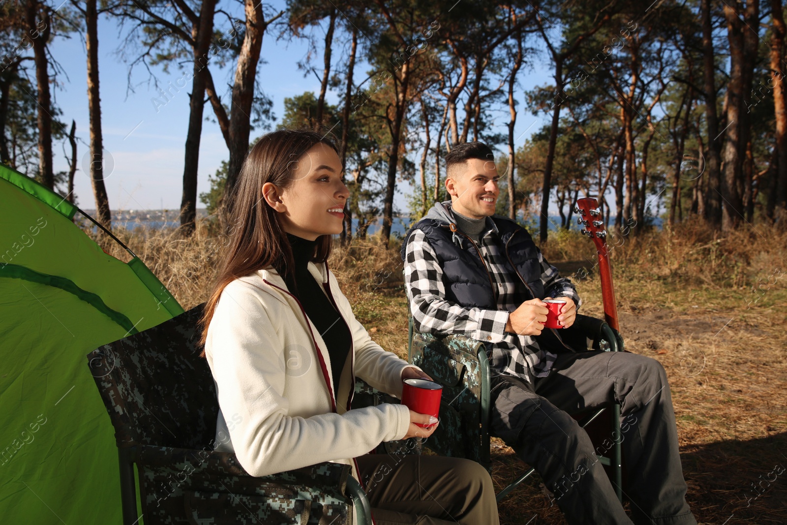 Photo of Couple resting in camping chairs and enjoying hot drink outdoors