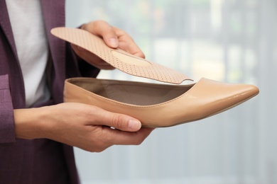 Photo of Woman putting orthopedic insole into shoe indoors, closeup. Foot care