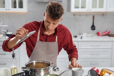 Photo of Man opening saucepan in messy kitchen. Many dirty dishware and utensils on table