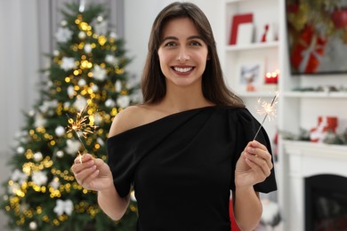 Photo of Portrait of smiling woman holding burning sparklers in room with Christmas decorations