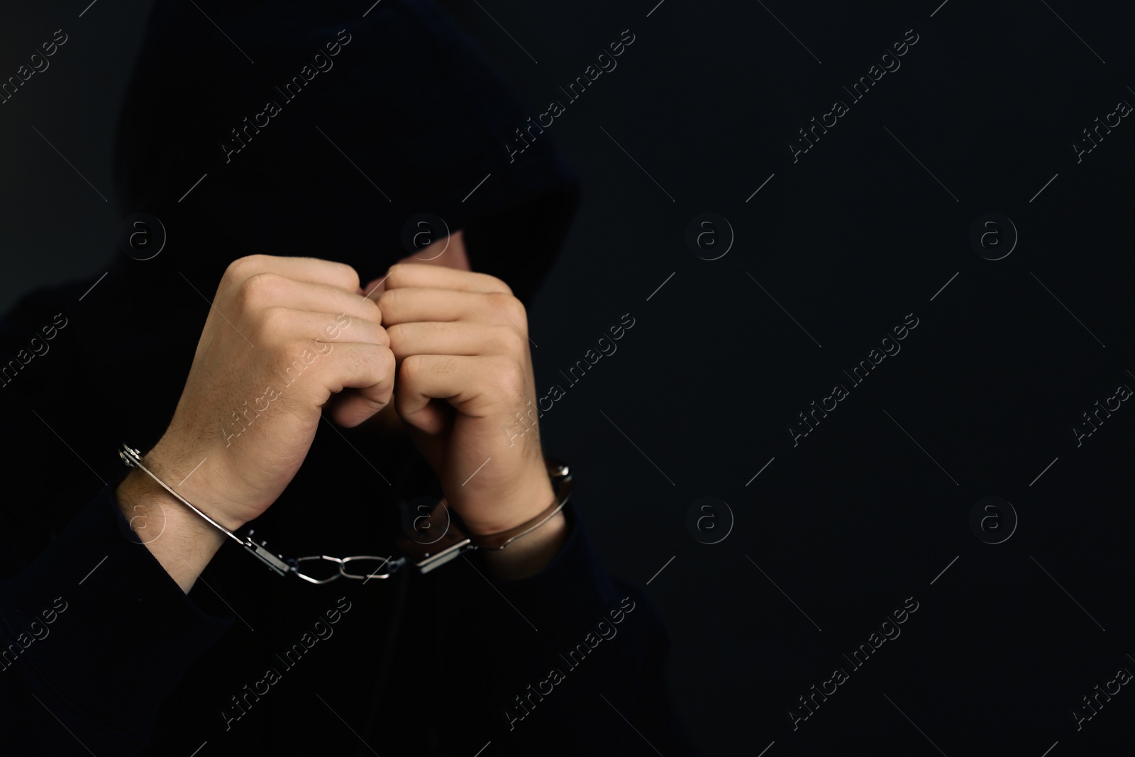 Photo of Man detained in handcuffs against dark background, space for text. Criminal law