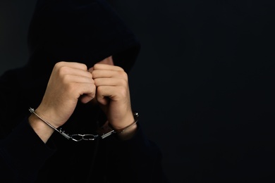 Photo of Man detained in handcuffs against dark background, space for text. Criminal law