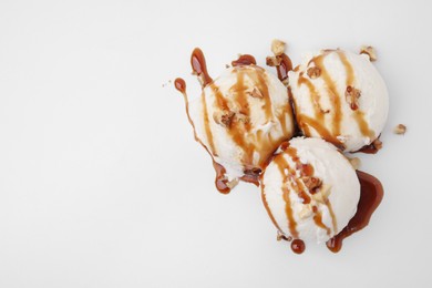 Photo of Scoops of ice cream with caramel sauce and nuts on white background, flat lay. Space for text