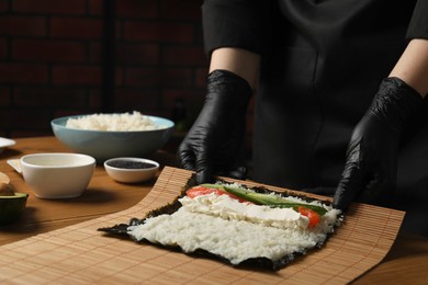 Photo of Chef in gloves making sushi roll at wooden table, closeup