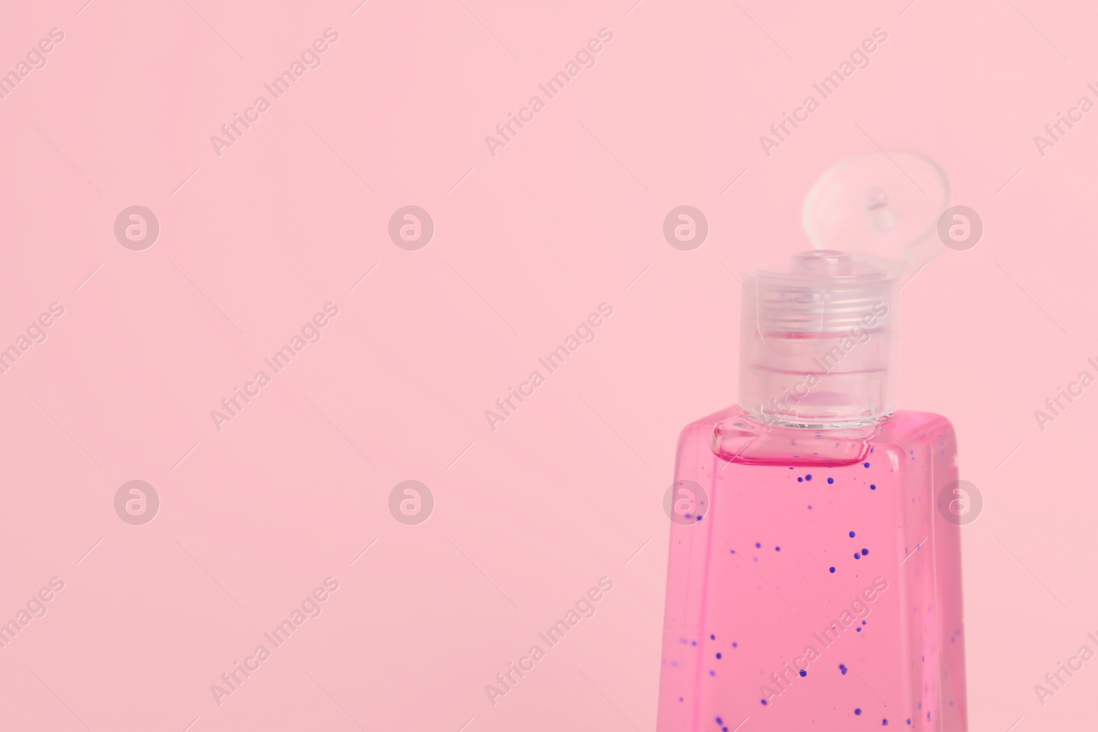 Photo of Bottle with antiseptic gel on pink background, closeup. Space for text