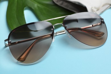 Photo of Stylish elegant sunglasses on light blue background, closeup