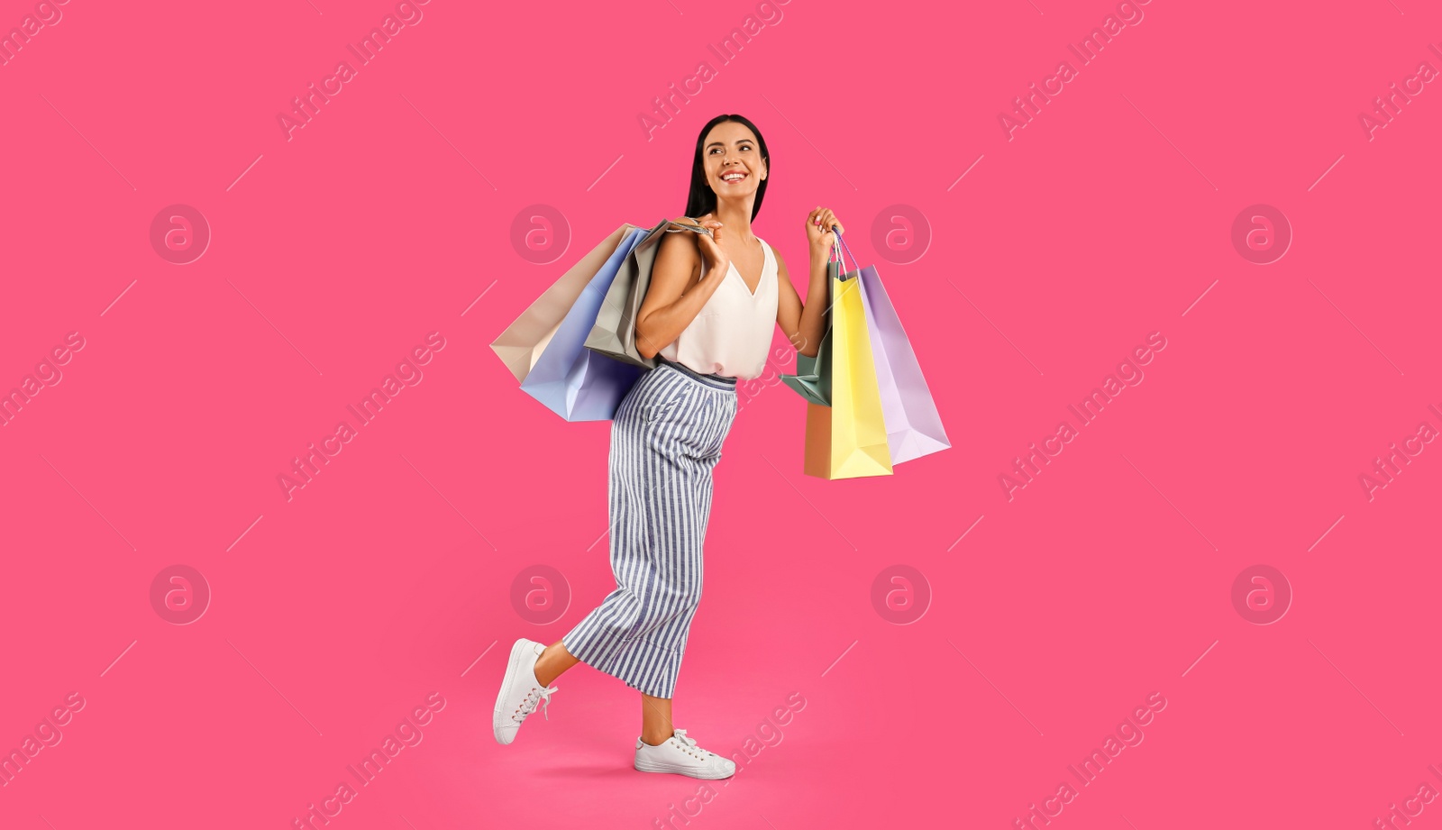 Photo of Beautiful young woman with paper shopping bags on pink background