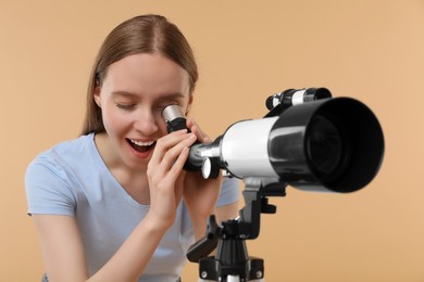 Photo of Young astronomer looking at stars through telescope on beige background