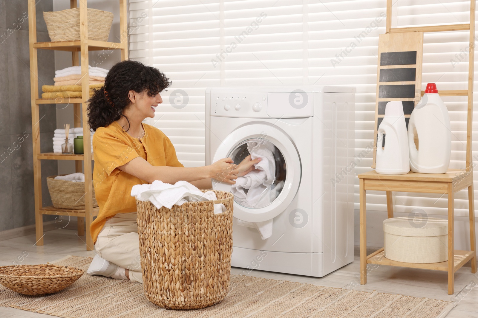 Photo of Happy woman putting laundry into washing machine indoors