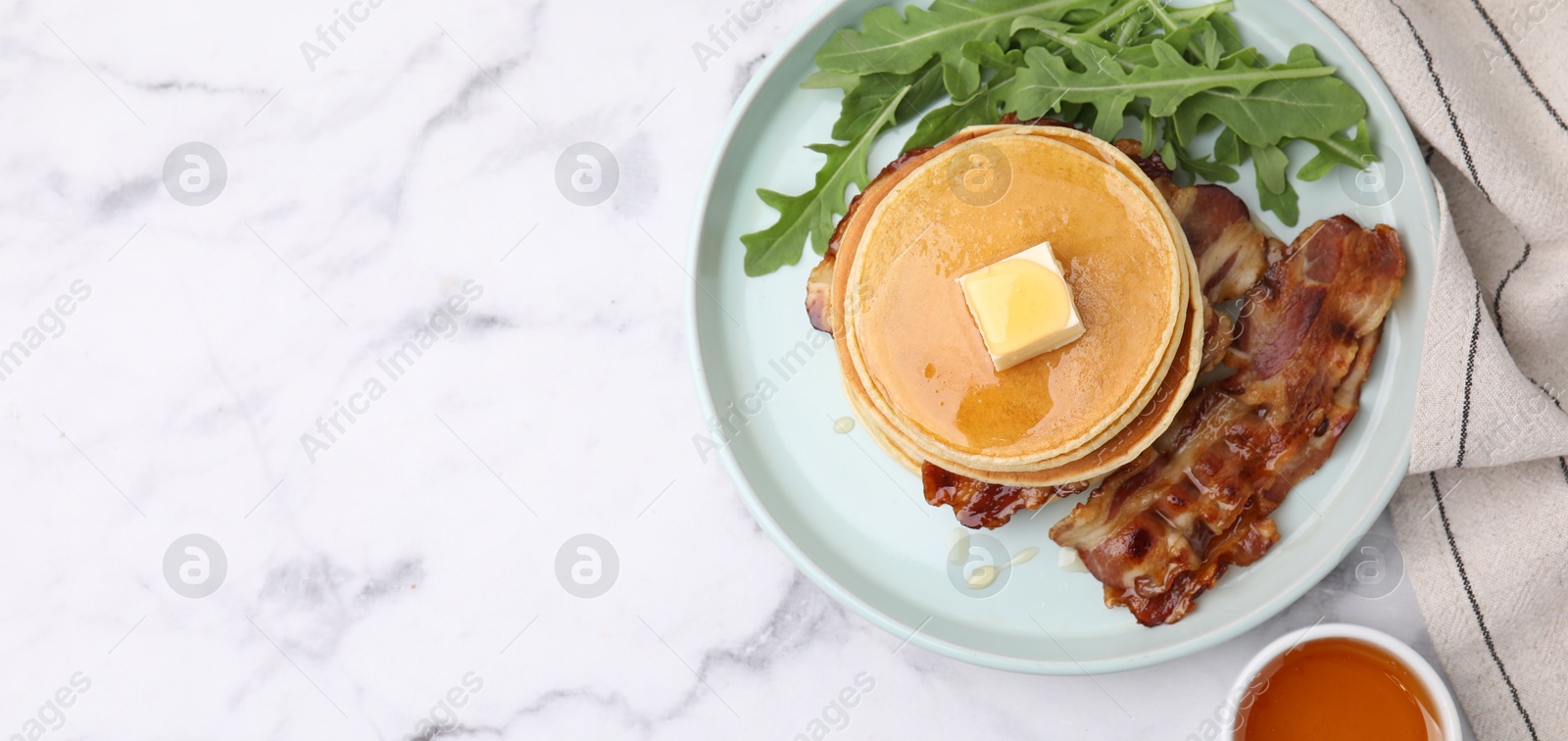 Photo of Tasty pancakes with butter, fried bacon and fresh arugula on white marble table, flat lay with space for text. Banner design