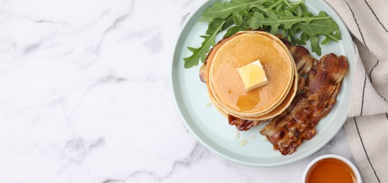Photo of Tasty pancakes with butter, fried bacon and fresh arugula on white marble table, flat lay with space for text. Banner design