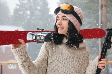 Photo of Young woman with skis wearing winter sport clothes and goggles outdoors