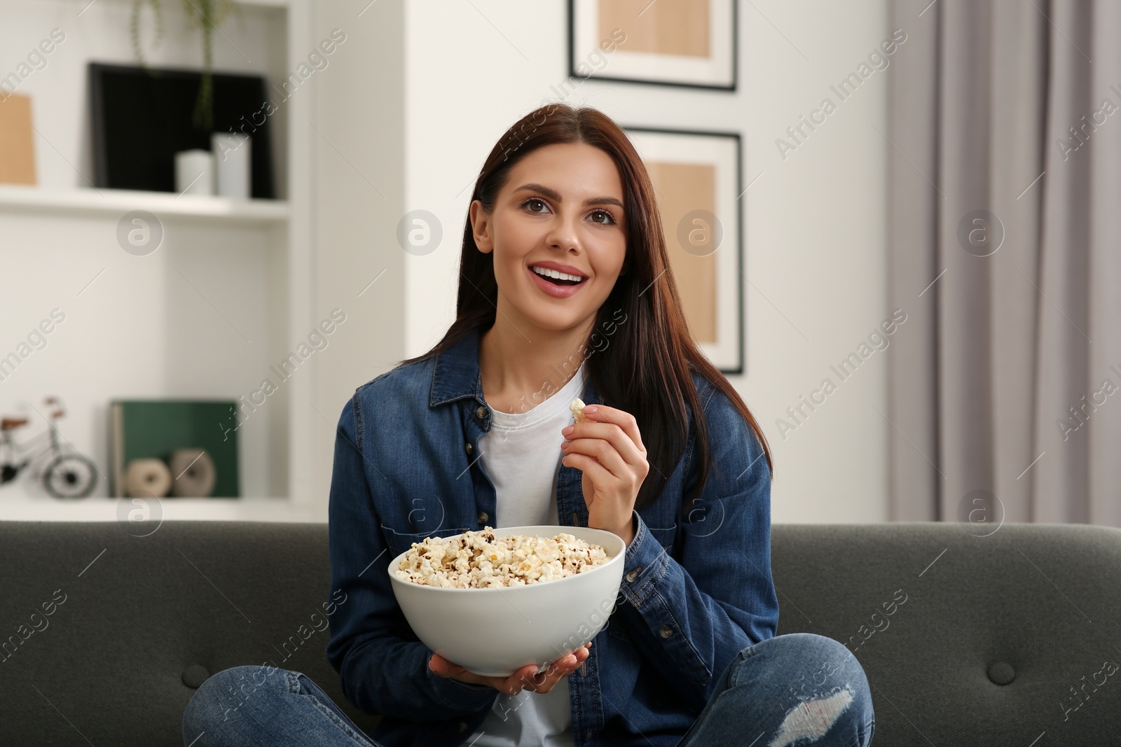 Photo of Happy woman with bowl of popcorn watching TV at home