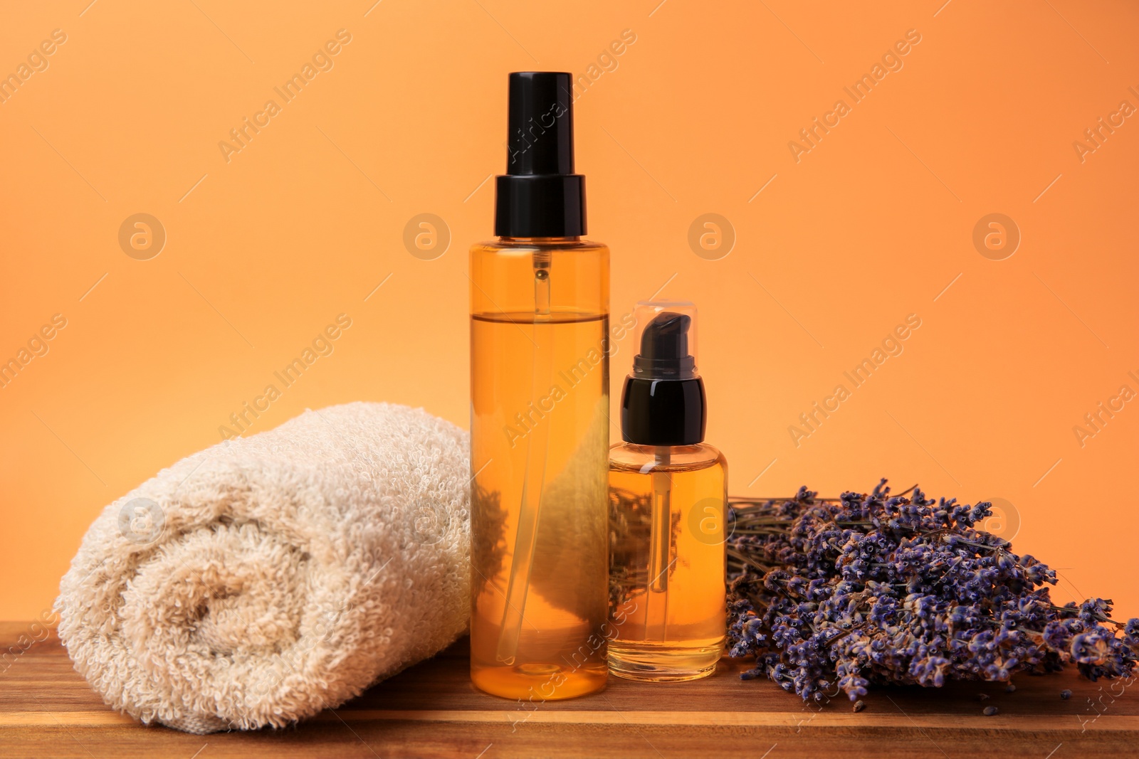 Photo of Bottles of cosmetic products, rolled towel and dry lavender flowers on orange background