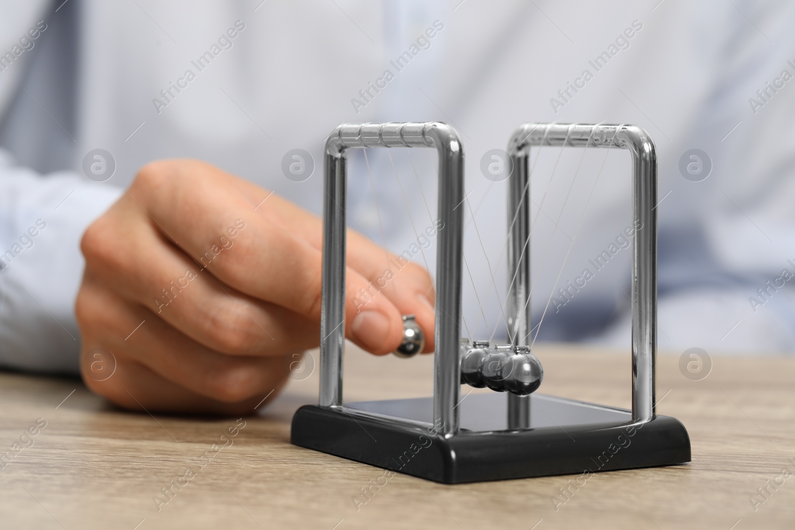 Photo of Man playing with Newton's cradle at wooden table, closeup. Physics law of energy conservation