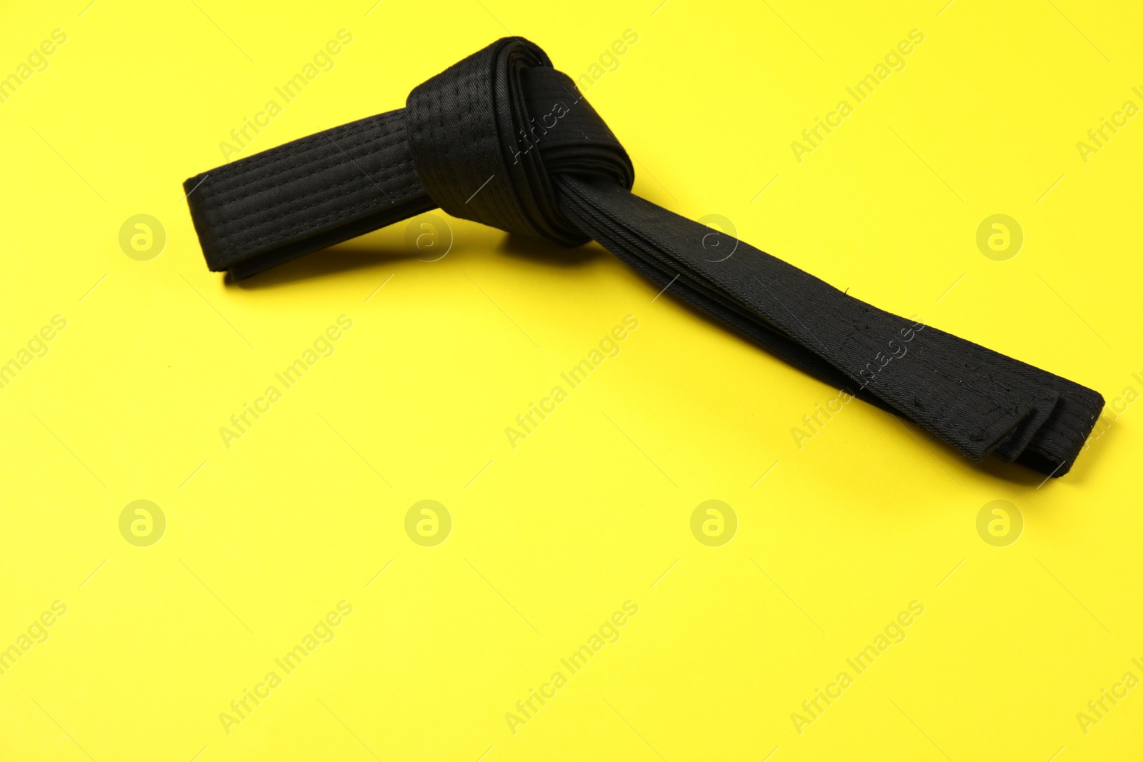 Photo of Black karate belt on yellow background, space for text