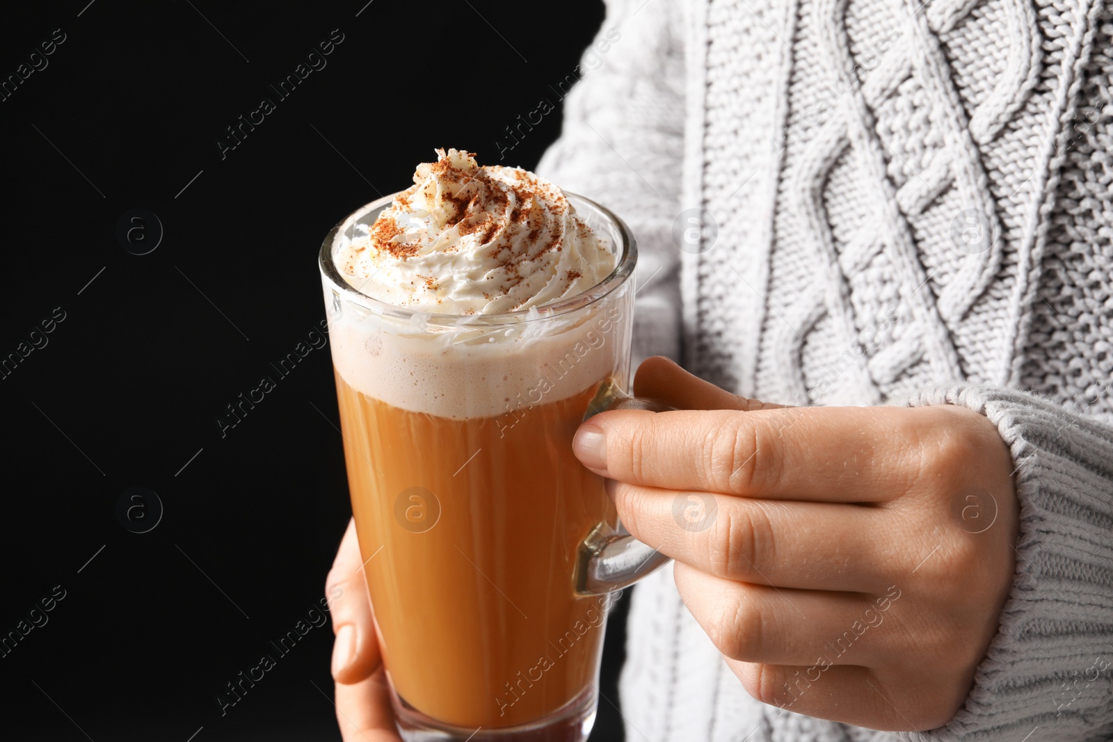 Photo of Woman holding glass cup with tasty pumpkin spice latte on black background, closeup