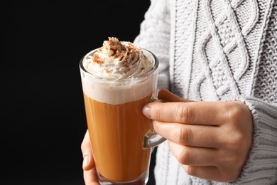 Woman holding glass cup with tasty pumpkin spice latte on black background, closeup