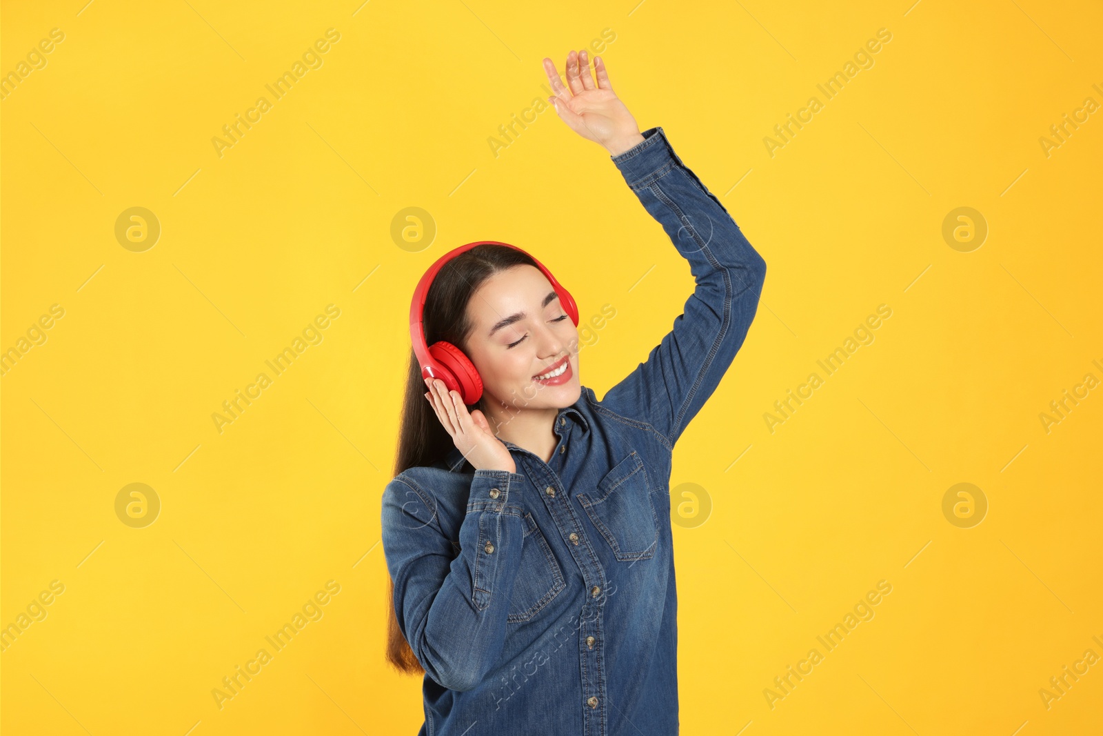 Photo of Happy woman in headphones listening music and dancing on orange background