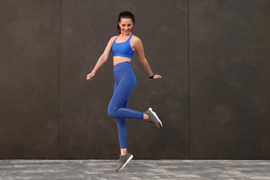 Photo of Beautiful woman in stylish sportswear jumping near black wall outdoors