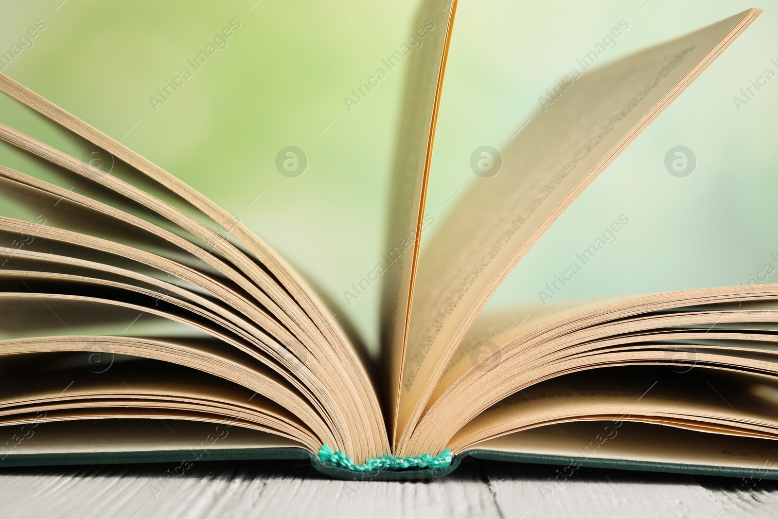 Photo of Open book on white wooden table against blurred green background, closeup