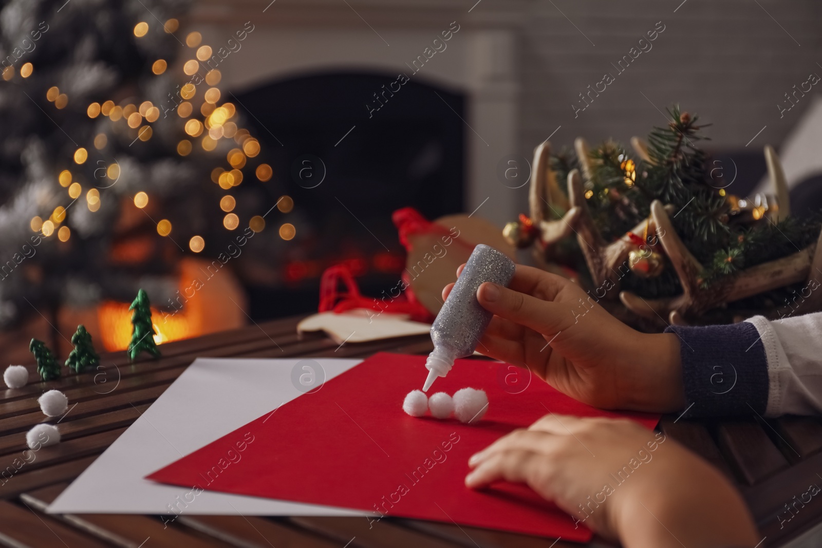 Photo of Little child making Christmas card at wooden table, closeup