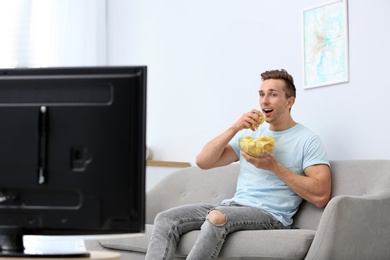 Photo of Man eating potato chips while watching TV in living room