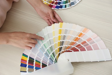 Photo of Female interior designer with color palette samples at wooden table, top view