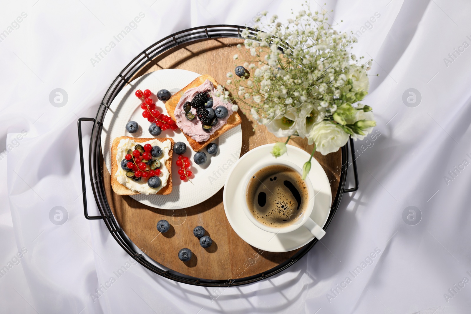 Photo of Tray with cup of coffee, cream cheese sandwiches and flowers on white fabric, top view